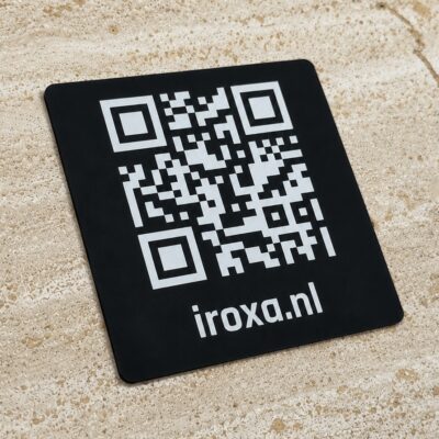Zwart metalen QR-code bordje met witte gravure in schuin aanzicht op travertin ondergrond